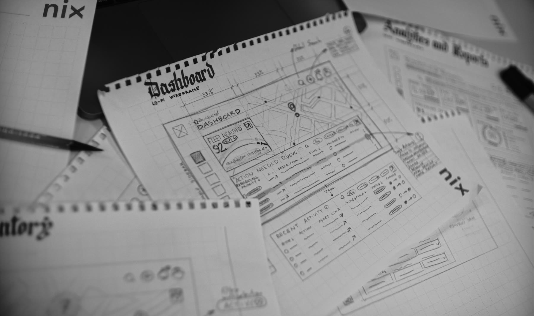 Hand-drawn wireframes on spiral pads, shot in black and white — sheets labelled Dashboard and Analytics and Reports, pencilled out beside the pencil that drew them